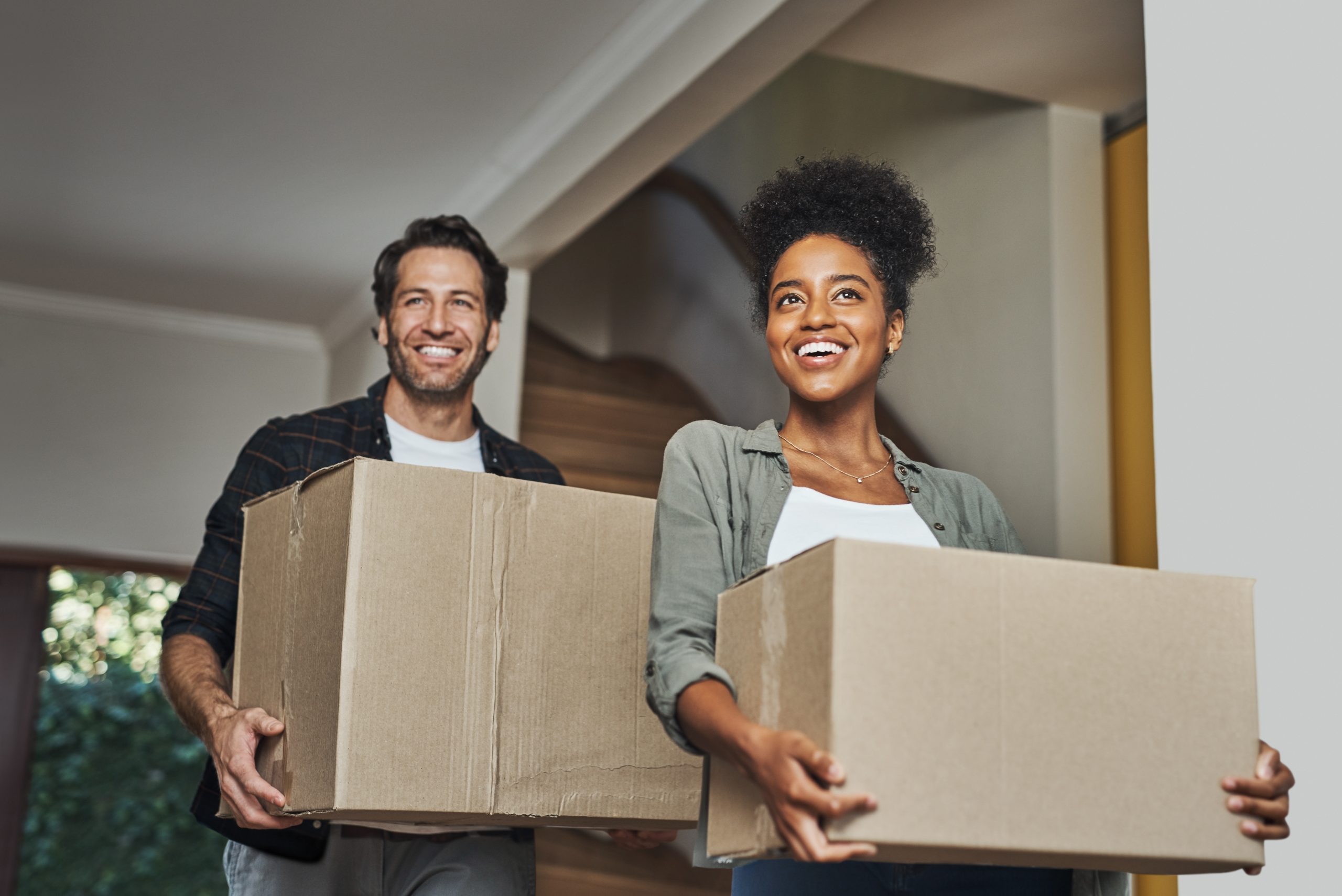 New house, moving and happy couple carrying boxes while feeling proud and excited about buying a house with a mortgage loan. Interracial husband and wife first time buyers unpacking in dream home.